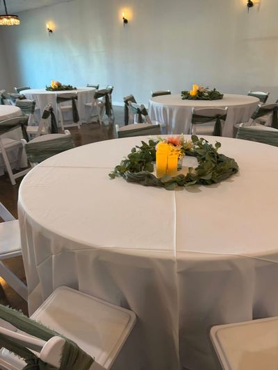 Wedding reception table with a greenery wreath, candle, and sage sashes
