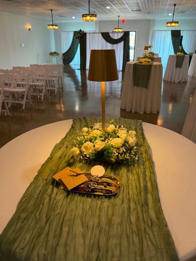 Reception table with a green runner, white roses, and lamp centerpiece