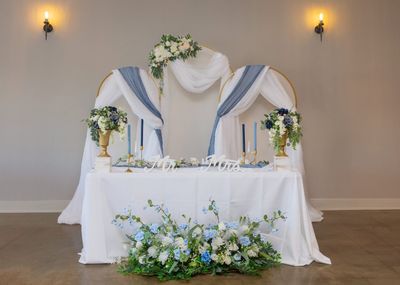Sweetheart table with a gold arch backdrop and blue florals